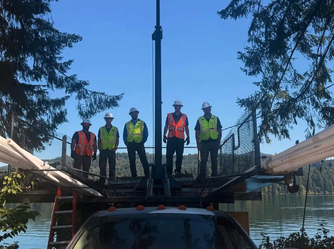 Aqua Pro Pump Service team standing on truck platform at a lakeside job site